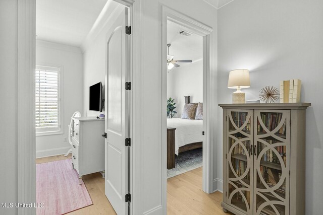 hallway featuring visible vents, crown molding, and light wood-style floors