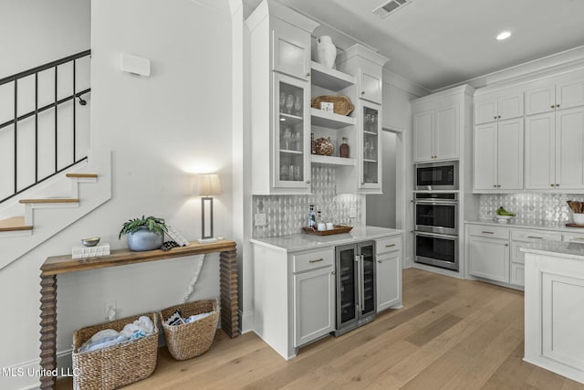 kitchen featuring visible vents, stainless steel double oven, wine cooler, light countertops, and built in microwave