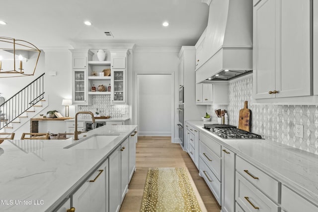 kitchen with open shelves, ornamental molding, stainless steel appliances, a sink, and custom range hood