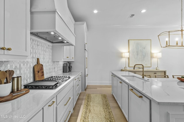 kitchen featuring a sink, ornamental molding, premium range hood, and stainless steel gas cooktop