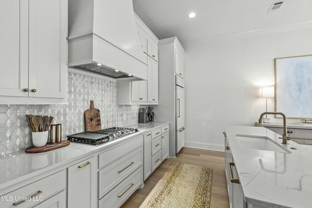 kitchen featuring visible vents, custom exhaust hood, a sink, stainless steel gas stovetop, and tasteful backsplash