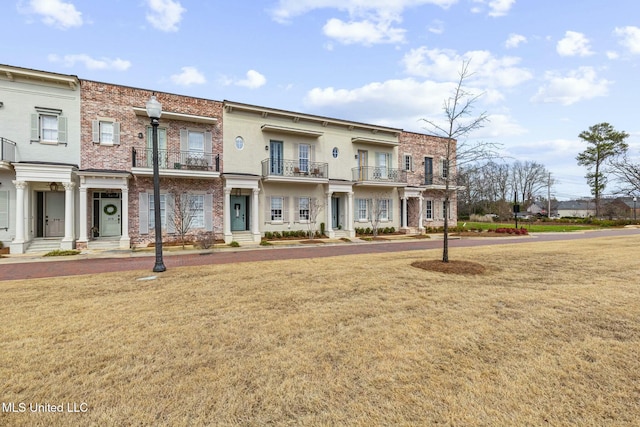 view of front of property with brick siding, a front lawn, and a balcony