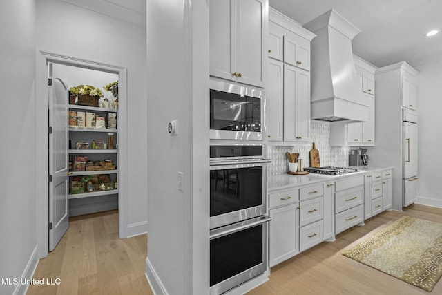 kitchen featuring light wood-style flooring, custom range hood, white cabinetry, appliances with stainless steel finishes, and light countertops