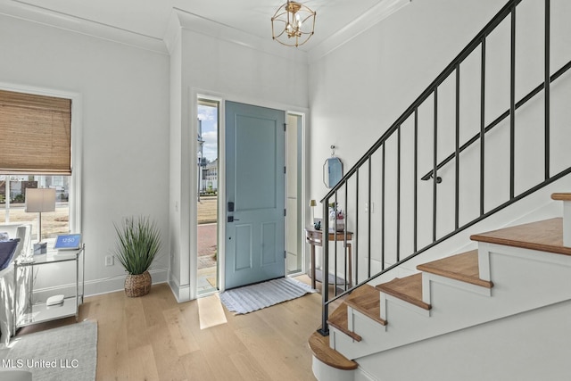 entrance foyer featuring a notable chandelier, stairway, wood finished floors, and ornamental molding