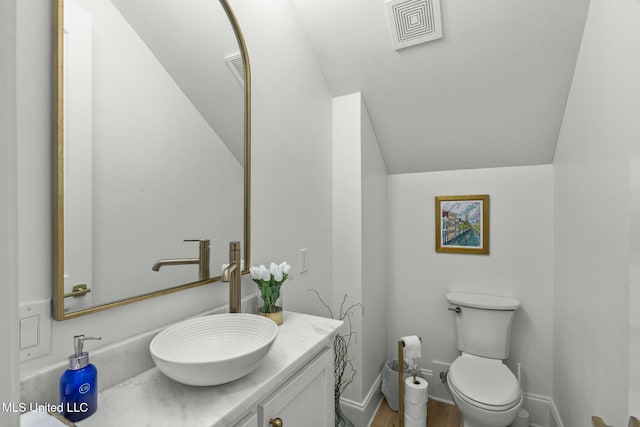 half bath with visible vents, baseboards, toilet, vaulted ceiling, and vanity