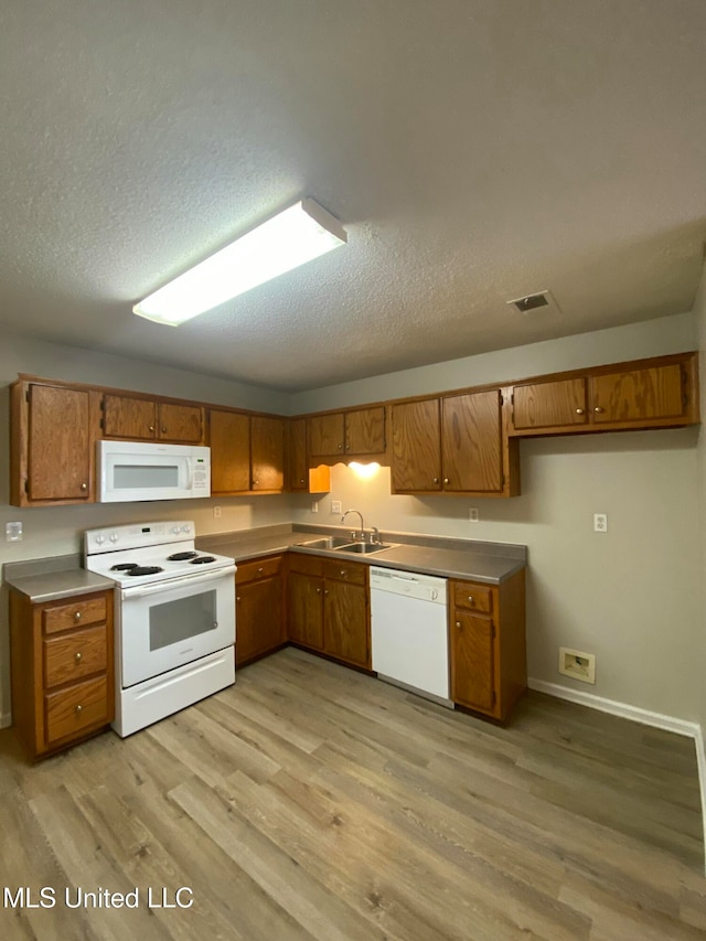 kitchen featuring light wood-type flooring, a textured ceiling, white appliances, and sink