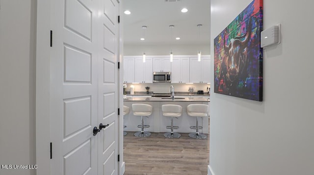 132 Markham Dr, Gulfport, MS 39507 - kitchen with stainless steel microwave, a kitchen breakfast bar, light wood-type flooring, recessed lighting, and white cabinetry