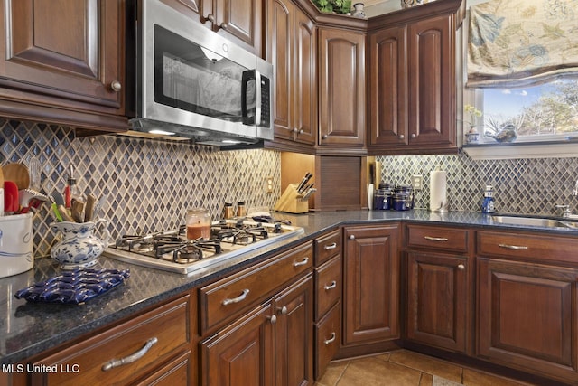 kitchen with backsplash, sink, dark stone countertops, light tile patterned floors, and appliances with stainless steel finishes