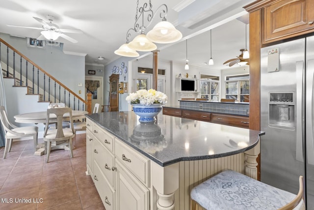 kitchen featuring stainless steel refrigerator with ice dispenser, dark stone counters, a kitchen bar, dark tile patterned flooring, and ornamental molding