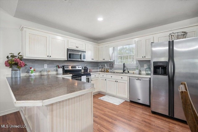 kitchen featuring sink, white cabinetry, appliances with stainless steel finishes, kitchen peninsula, and hardwood / wood-style floors