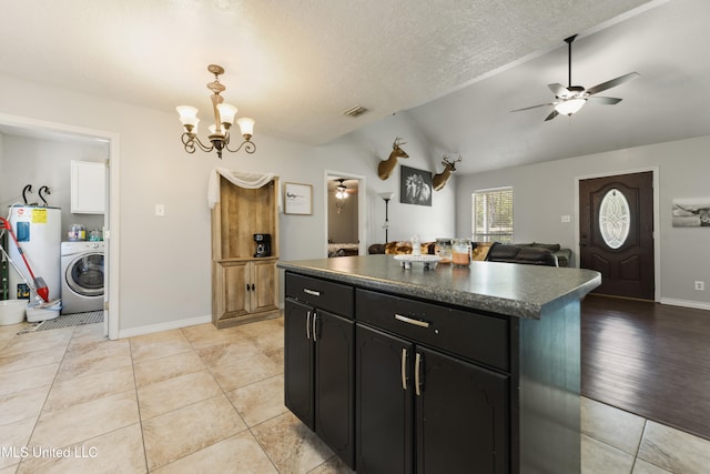 kitchen featuring electric water heater, ceiling fan with notable chandelier, vaulted ceiling, a kitchen island, and washer / dryer