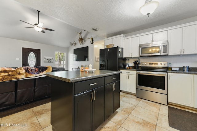 kitchen featuring appliances with stainless steel finishes, backsplash, vaulted ceiling, light tile patterned floors, and a center island