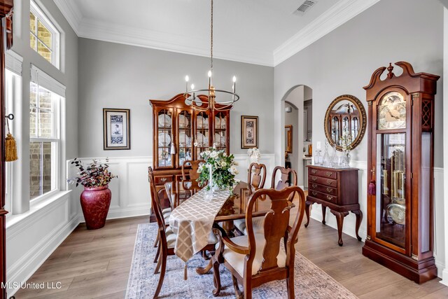 12578 Alphabet Rd, Gulfport, MS 39503 - dining space featuring arched walkways, a chandelier, crown molding, light wood-type flooring, and wainscoting