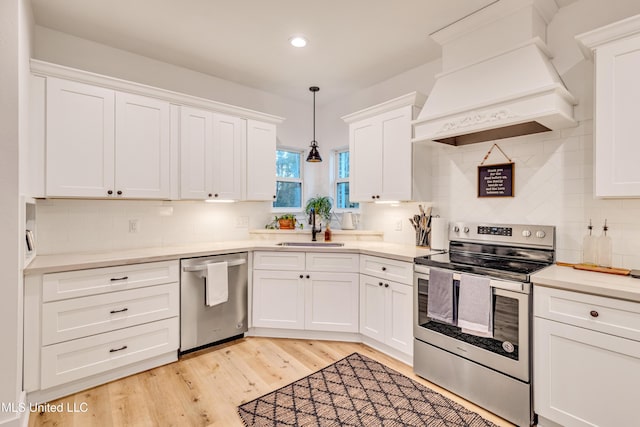 kitchen featuring white cabinetry, sink, stainless steel appliances, decorative light fixtures, and custom range hood