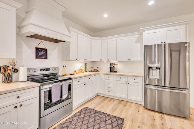 kitchen featuring tasteful backsplash, stainless steel appliances, white cabinetry, and premium range hood