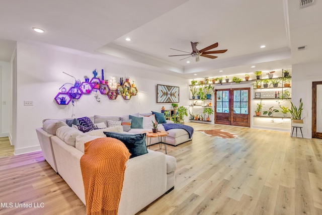 living room with ceiling fan, light hardwood / wood-style floors, french doors, and a tray ceiling