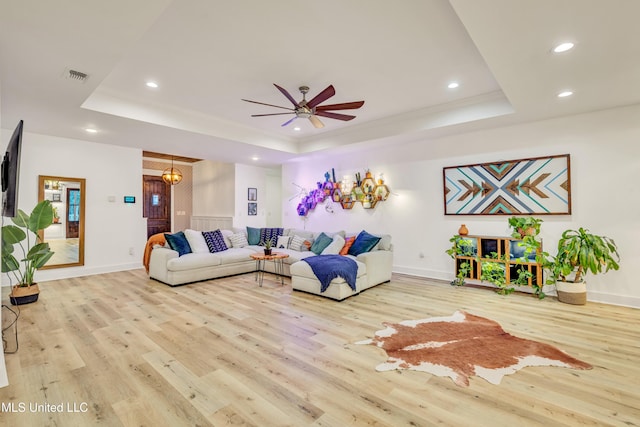 living room featuring ceiling fan with notable chandelier, light hardwood / wood-style floors, a raised ceiling, and crown molding