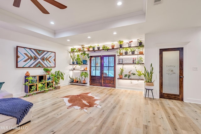 interior space with light hardwood / wood-style floors, a raised ceiling, crown molding, and french doors