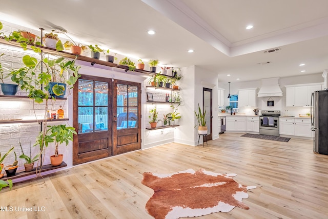 foyer entrance featuring a tray ceiling, french doors, ornamental molding, and light wood-type flooring