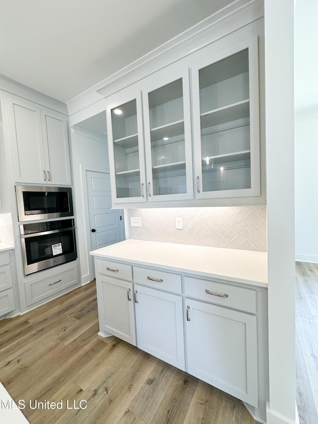 kitchen with built in microwave, light wood-style flooring, stainless steel oven, and backsplash