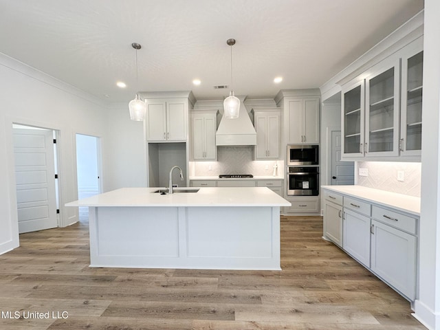 kitchen with appliances with stainless steel finishes, custom range hood, a sink, and light wood finished floors