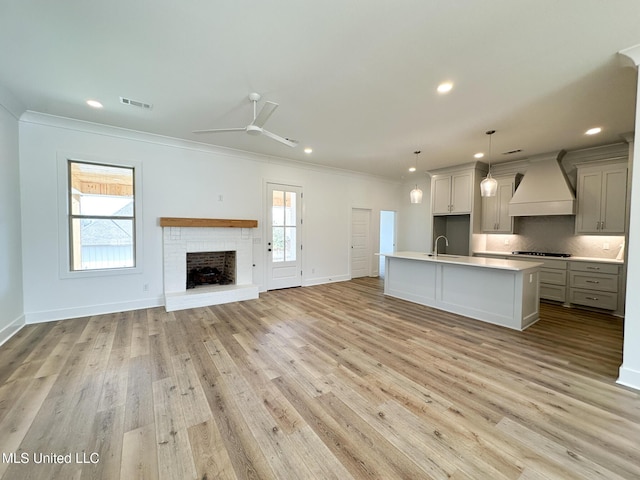 kitchen with tasteful backsplash, an island with sink, custom range hood, open floor plan, and a sink