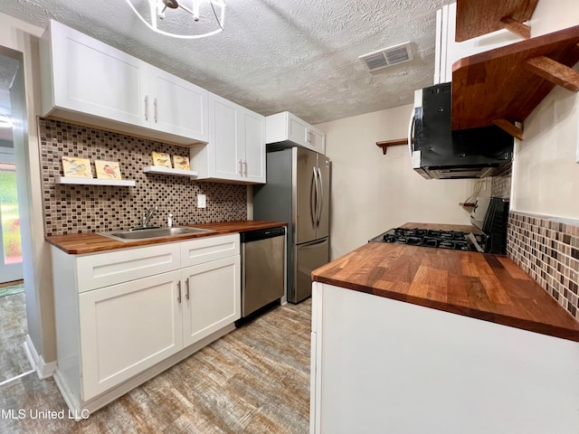 kitchen with tasteful backsplash, white cabinetry, wooden counters, and appliances with stainless steel finishes