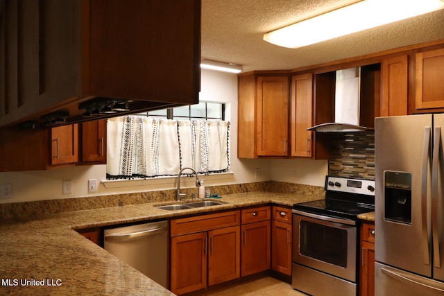 kitchen with wall chimney range hood, light stone countertops, appliances with stainless steel finishes, sink, and a textured ceiling