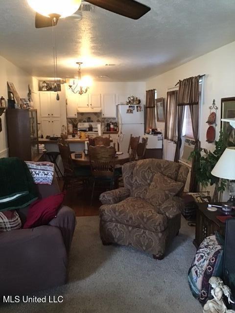 carpeted living room with ceiling fan with notable chandelier