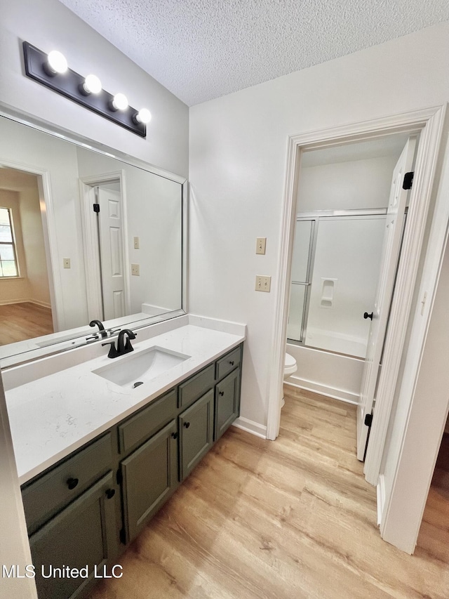 7164 Kimlee Cv, Southaven, MS 38671 - bathroom featuring vanity, wood finished floors, toilet, a textured ceiling, and bath / shower combo with glass door