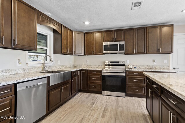 kitchen with a textured ceiling, sink, light wood-type flooring, appliances with stainless steel finishes, and dark brown cabinetry