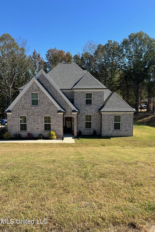 view of front facade featuring brick siding, a front yard, and roof with shingles