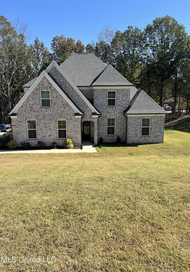 view of front facade featuring roof with shingles, a front lawn, and brick siding