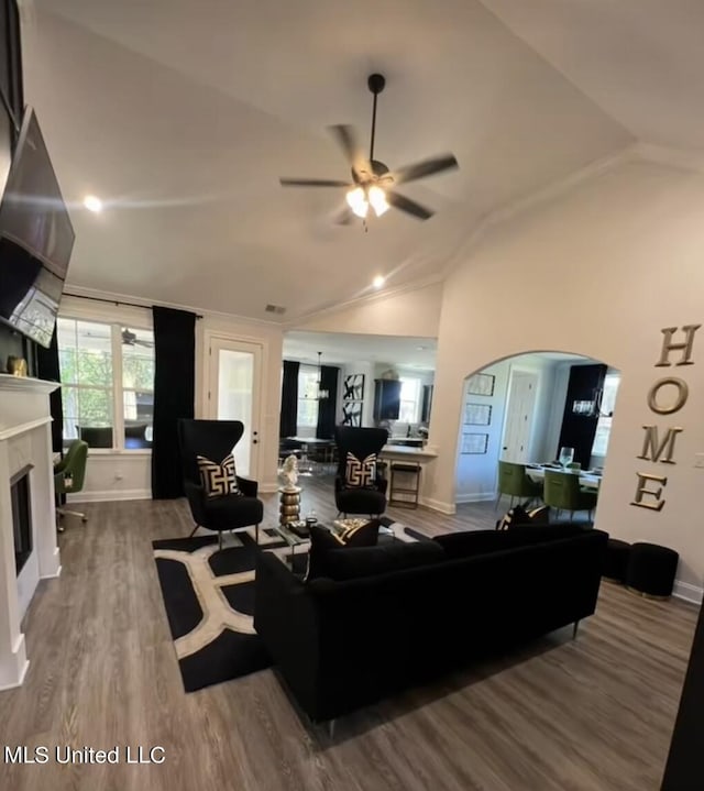 living room featuring ceiling fan, arched walkways, a tiled fireplace, baseboards, and vaulted ceiling