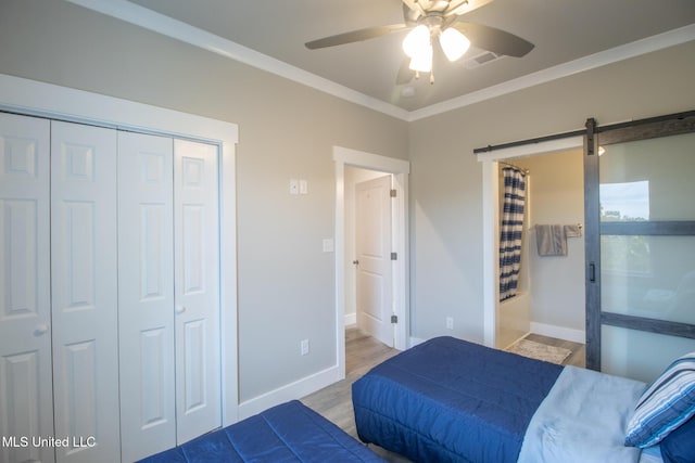 bedroom with a barn door, baseboards, light wood-style floors, ornamental molding, and a closet