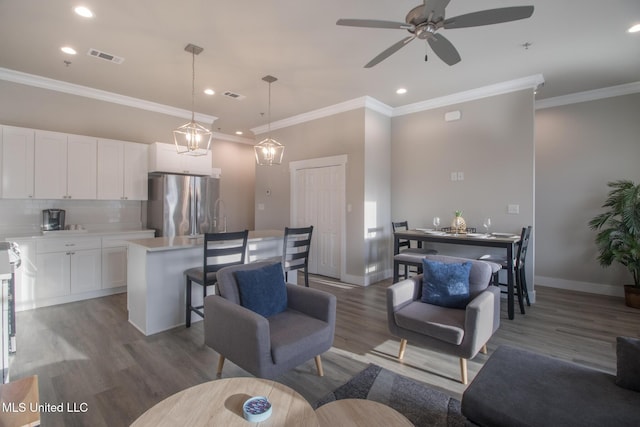 living room featuring visible vents, baseboards, wood finished floors, and ornamental molding