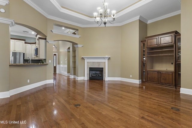 5578 E Diamondhead Dr, Diamondhead, MS 39525 - unfurnished living room featuring arched walkways, dark wood-style floors, crown molding, a tiled fireplace, and a chandelier