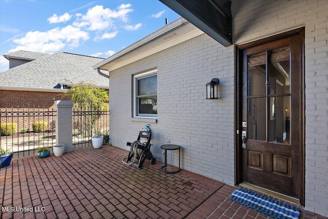 doorway to property featuring a patio, brick siding, and fence