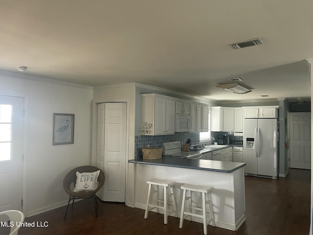 kitchen featuring a peninsula, white appliances, dark wood-style flooring, ornamental molding, and backsplash