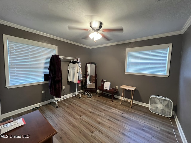 interior space with ornamental molding, a ceiling fan, a textured ceiling, wood finished floors, and baseboards