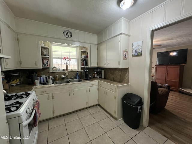 kitchen featuring a sink, white range with gas cooktop, light countertops, open shelves, and tasteful backsplash