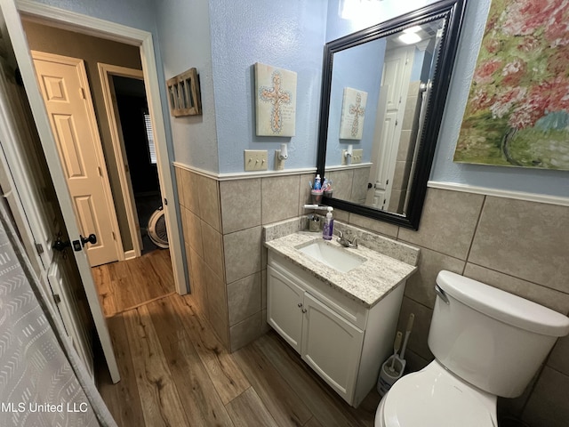 bathroom featuring toilet, wood finished floors, vanity, tile walls, and wainscoting