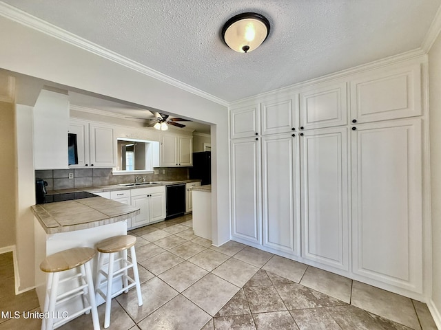 kitchen featuring black appliances, tile counters, a kitchen bar, white cabinetry, and a sink