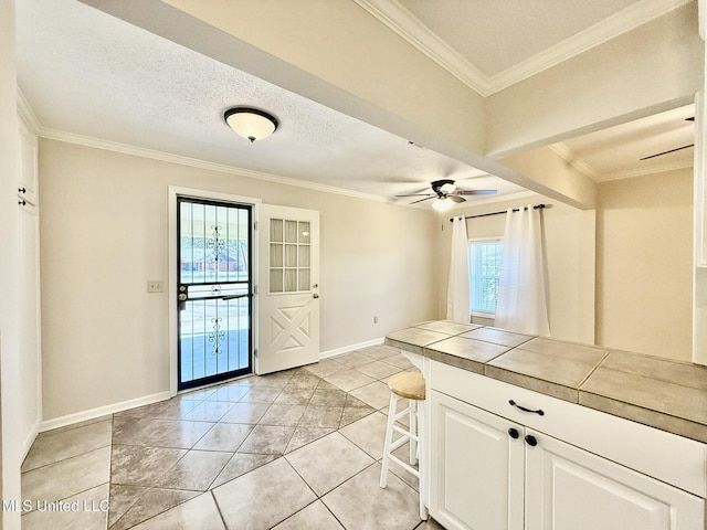 kitchen featuring a textured ceiling, white cabinetry, a breakfast bar area, crown molding, and tile counters