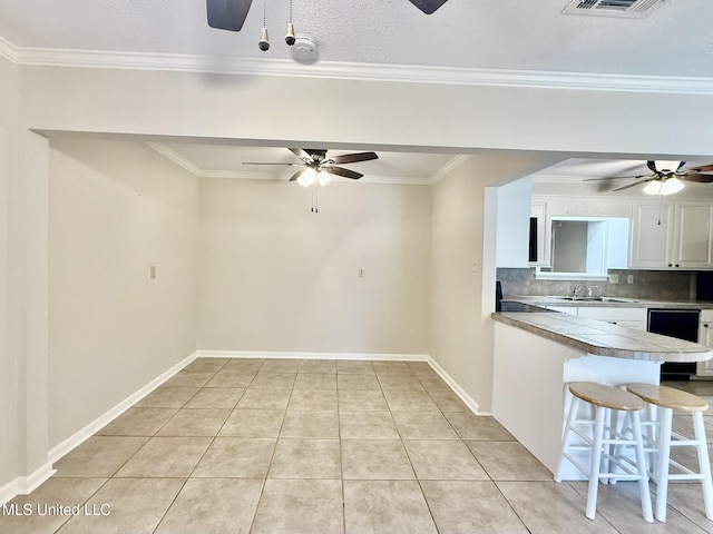 kitchen featuring a breakfast bar area, light tile patterned floors, ceiling fan, decorative backsplash, and white cabinets