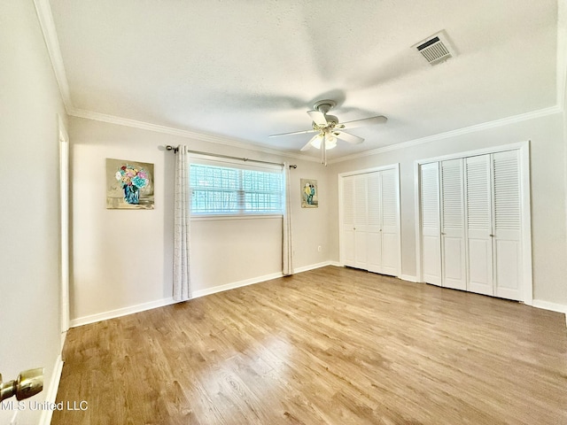 unfurnished bedroom with visible vents, two closets, crown molding, baseboards, and wood finished floors