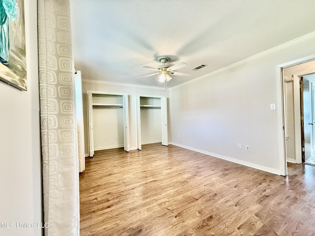 unfurnished bedroom with wood finished floors, baseboards, visible vents, crown molding, and two closets