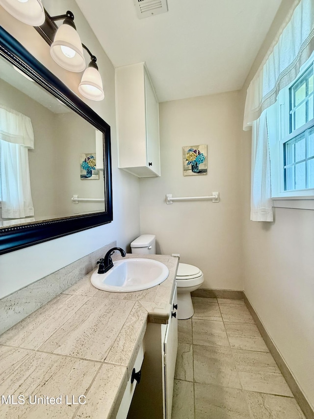 half bath featuring vanity, toilet, visible vents, and baseboards