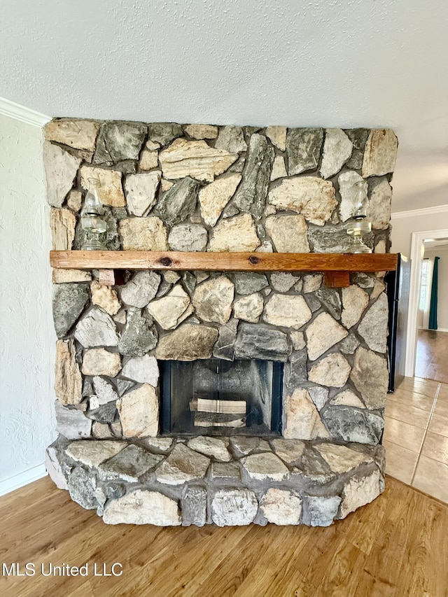 room details featuring crown molding, wood finished floors, a stone fireplace, a textured wall, and a textured ceiling