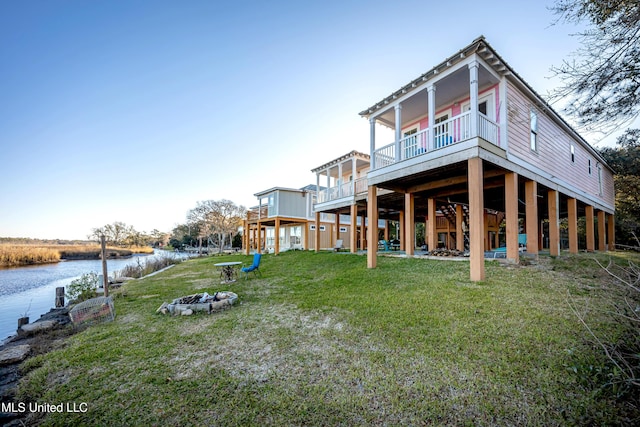 back of property with a lawn, an outdoor fire pit, and a deck with water view